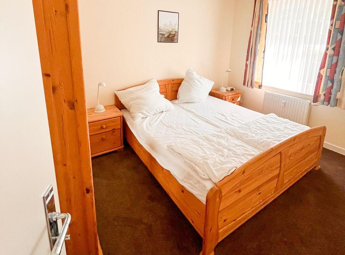 Schlafzimmer mit Holzbett, Nachttischen und Fenster.