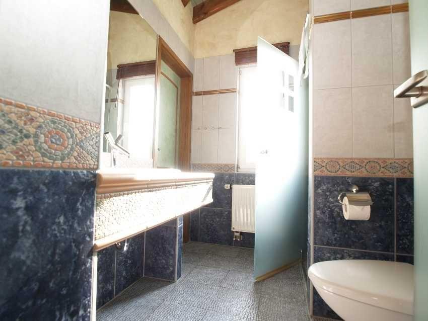 Badezimmer mit Waschtisch, Toilette und Dusche. Wandfliesen und Mosaikverzierung.
