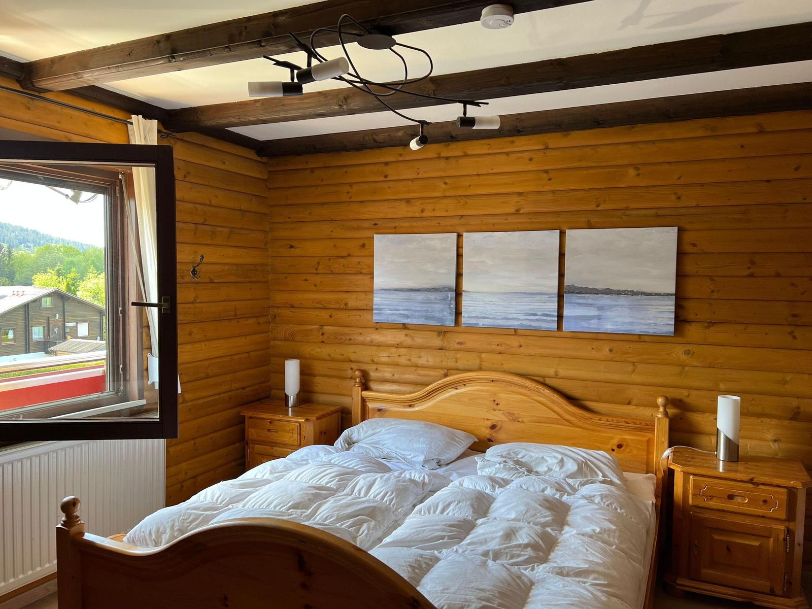 Bedroom with wooden walls, bed, nightstands, and window view of landscape.
