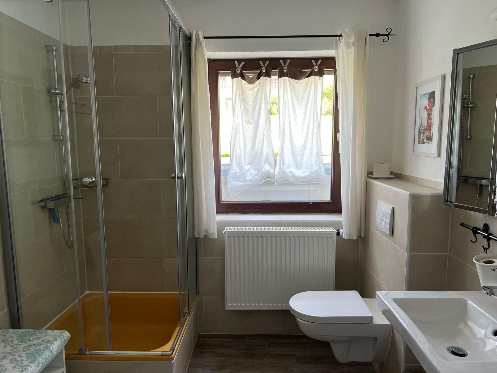 Bathroom with shower, toilet, and sink. Window with curtains and radiator.