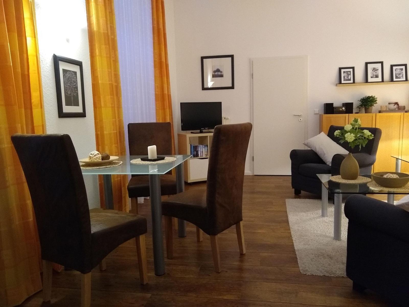 Wohn- und Essbereich mit Glas-Tisch, Stühlen, Sofa und TV.