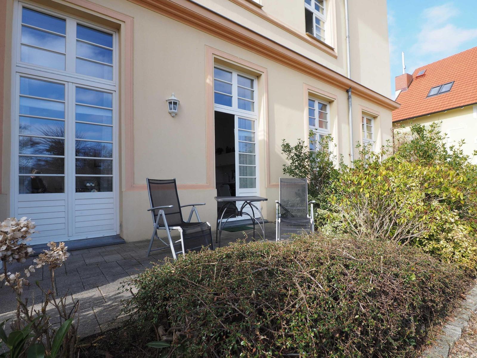 Terrasse mit zwei Stühlen und Tisch vor einem Haus mit Fenstern.