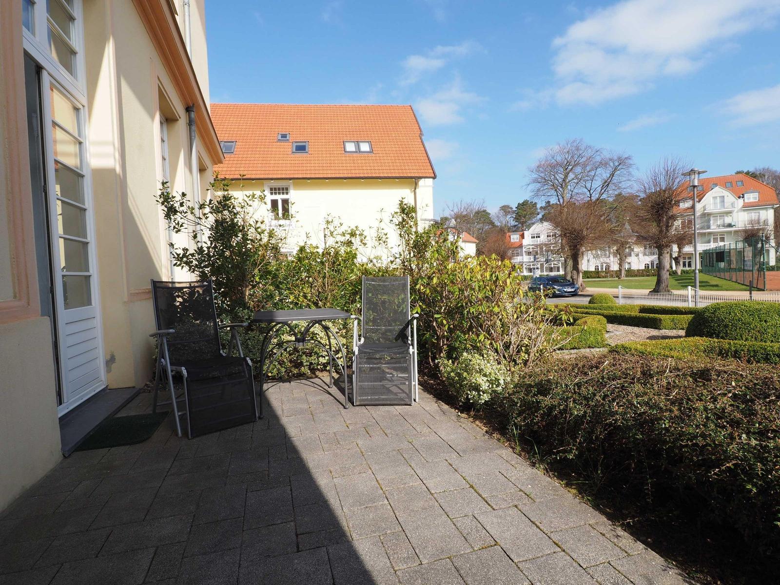Terrasse mit Tisch und zwei Stühlen neben einem Haus mit Garten.