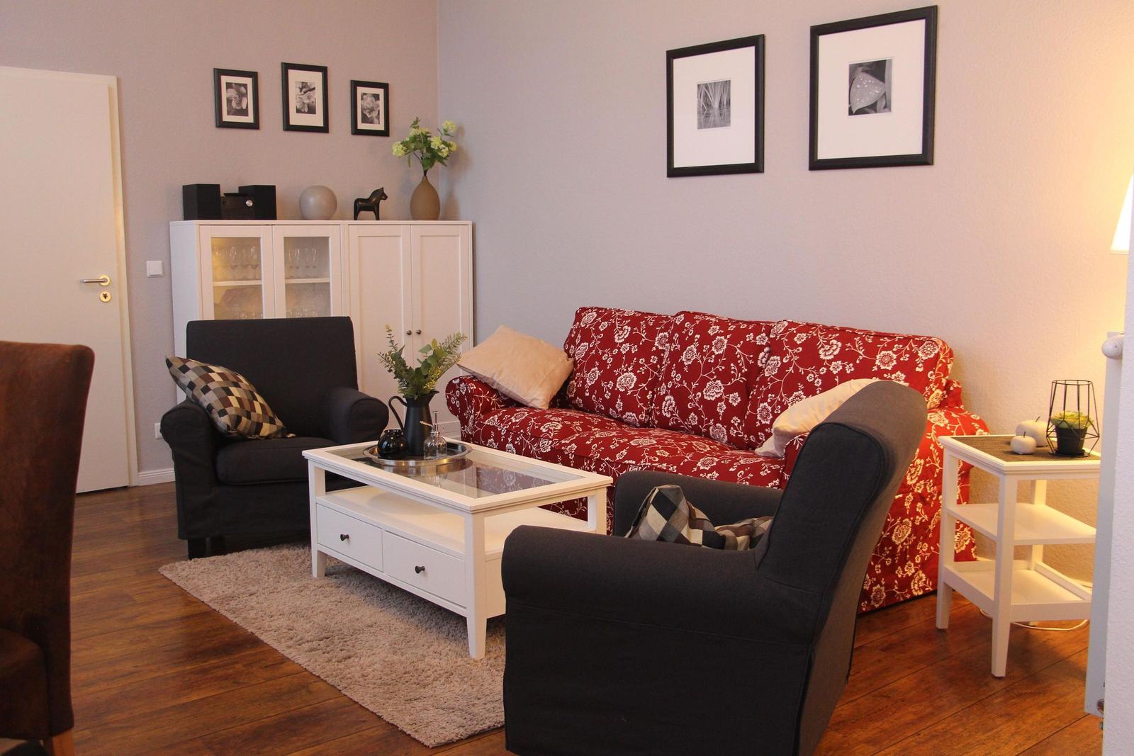 Wohnzimmer mit rotem Sofa, zwei schwarzen Sesseln und weißem Couchtisch.