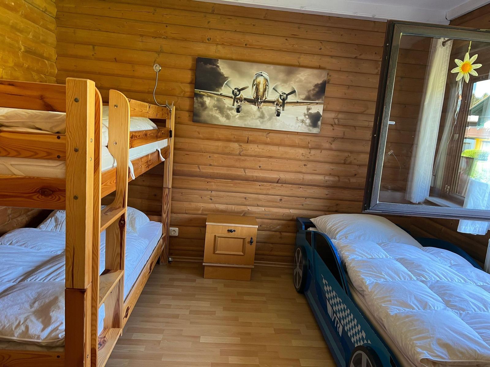 Room with wood wall, bunk bed, and car bed. Wall picture shows airplane.