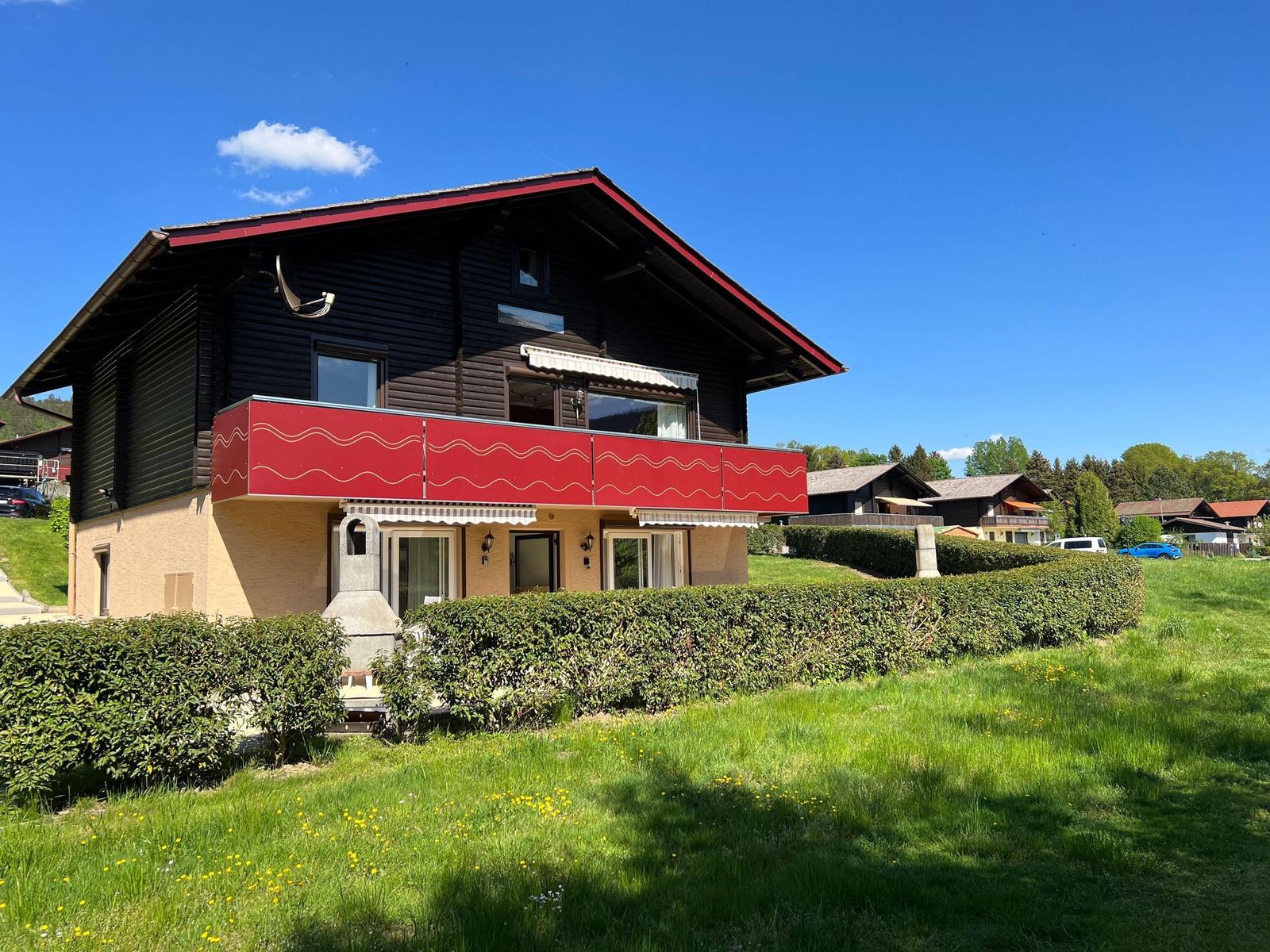 House with red balcony and green lawn under a clear sky.