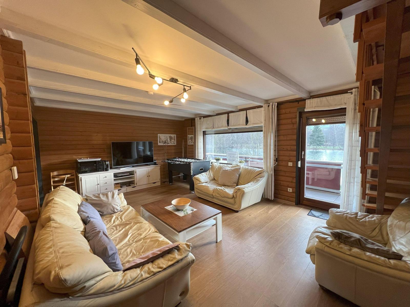 Living room with sofa, coffee table, and TV. Wooden walls and terrace door to the lake.