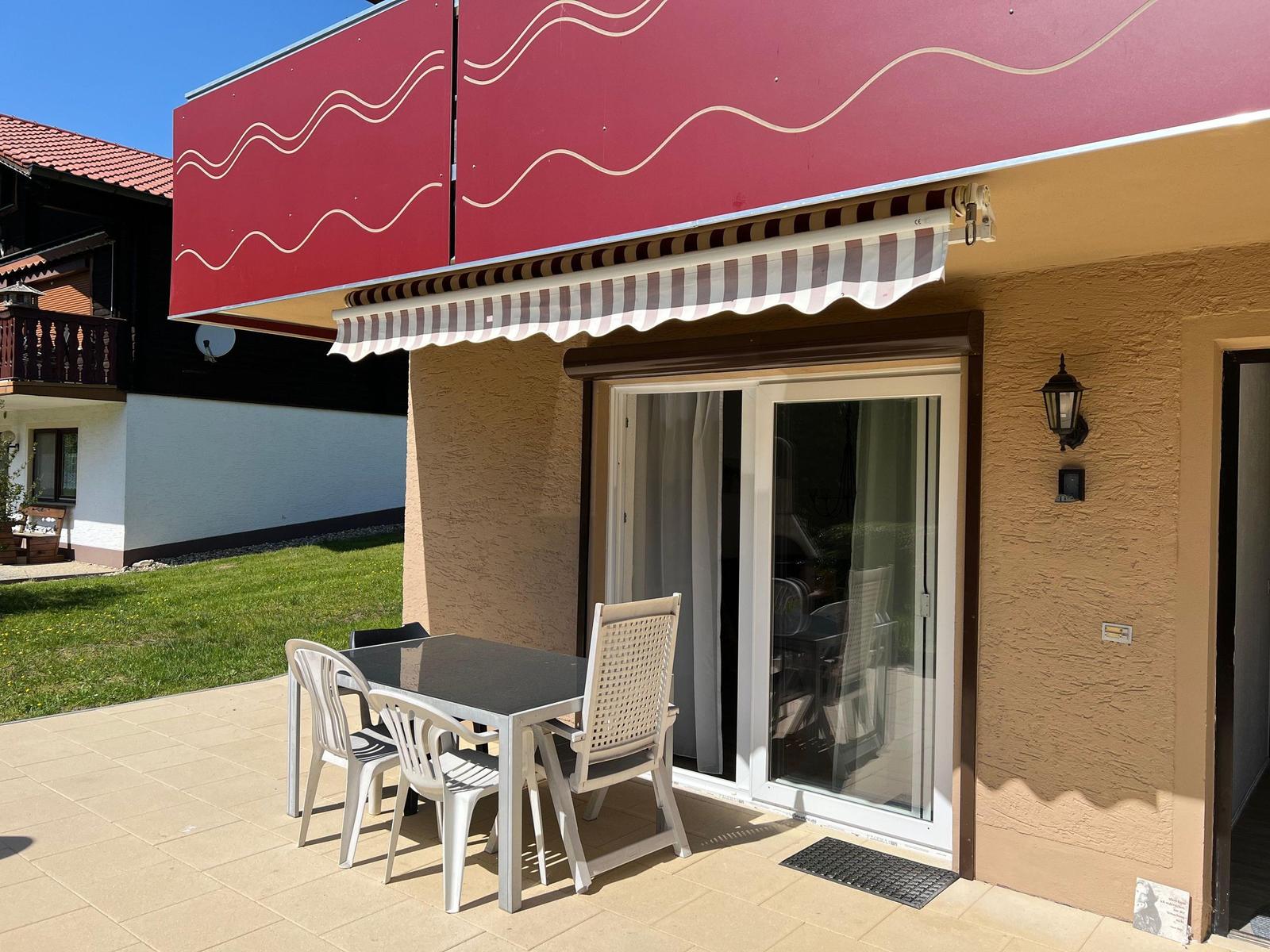 Terrace with table and chairs under awning. Sliding door leads into the house.