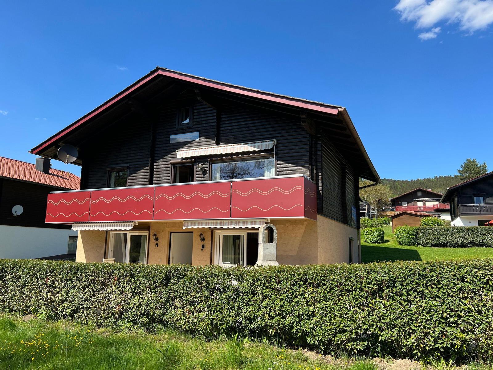 A two-story house with a red balcony and green hedge fence.