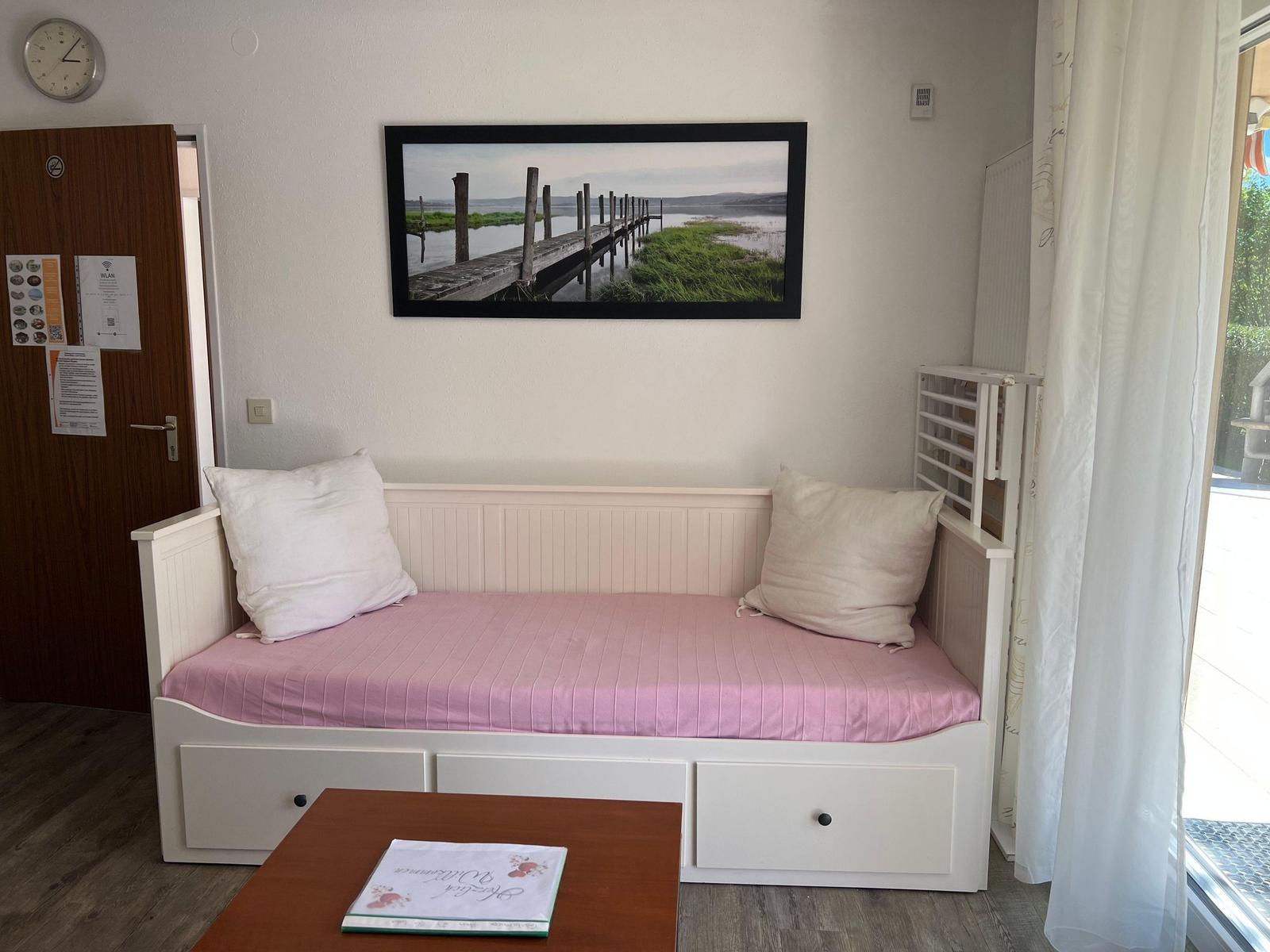 A bedroom with a white bed, pink bedding, and wall art of a pier.