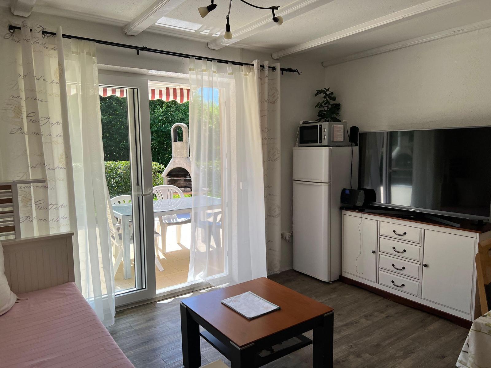 Living room with kitchenette, TV, and terrace with grill.