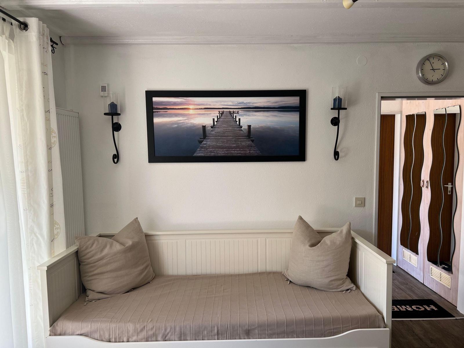 A sofa with cushions under a picture on the wall. A door leads into a hallway.