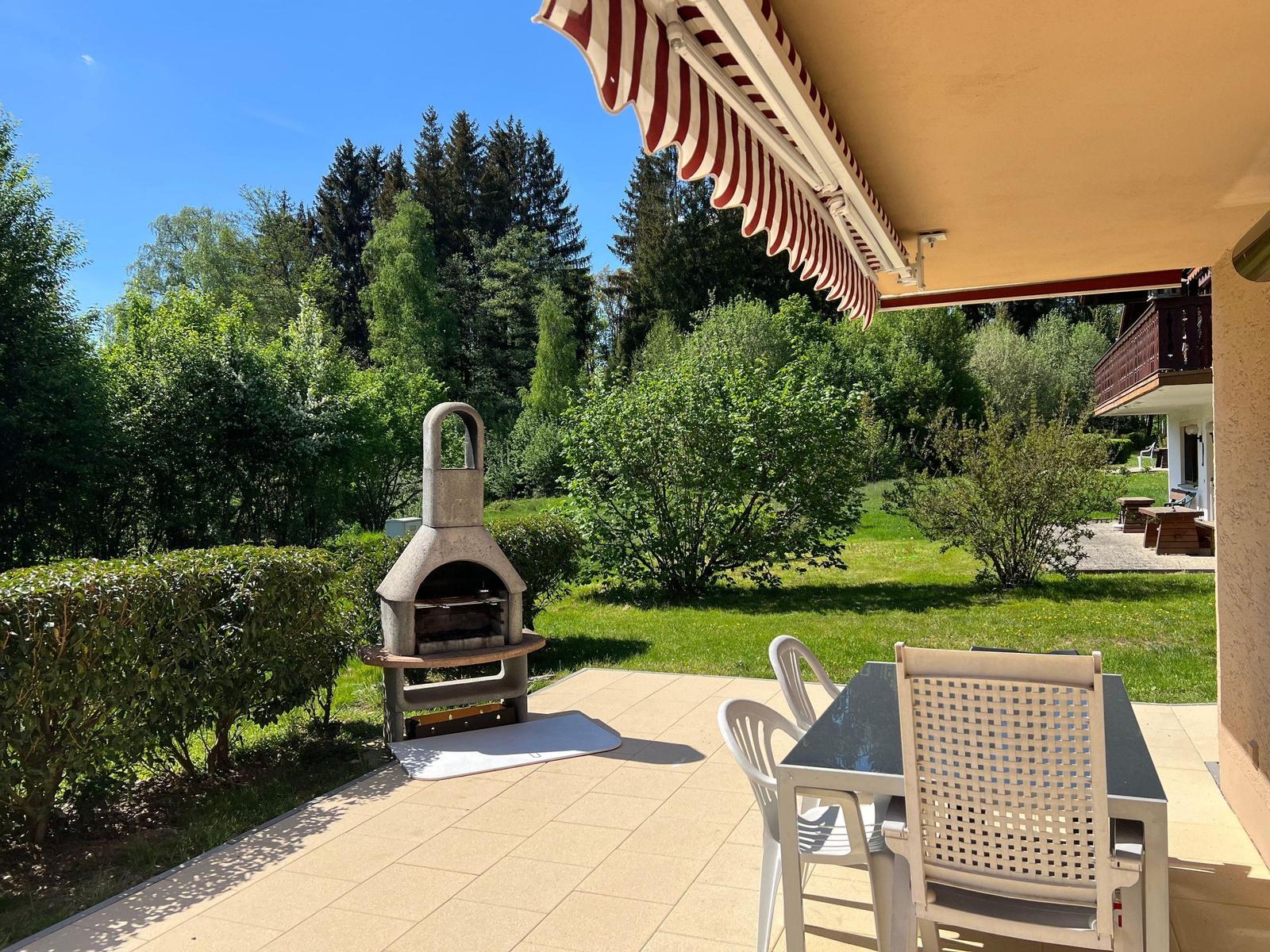 Terrace with table, chairs, and stone oven. View of green garden and forest.