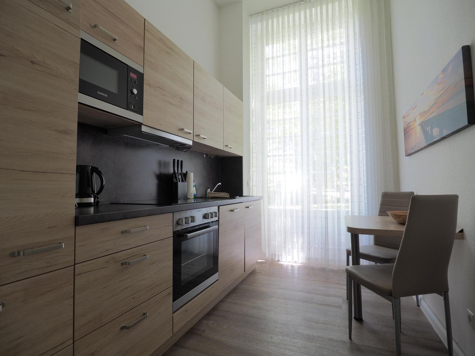 Küche mit Essbereich, Holzmöbeln und Fenster mit Vorhängen.
