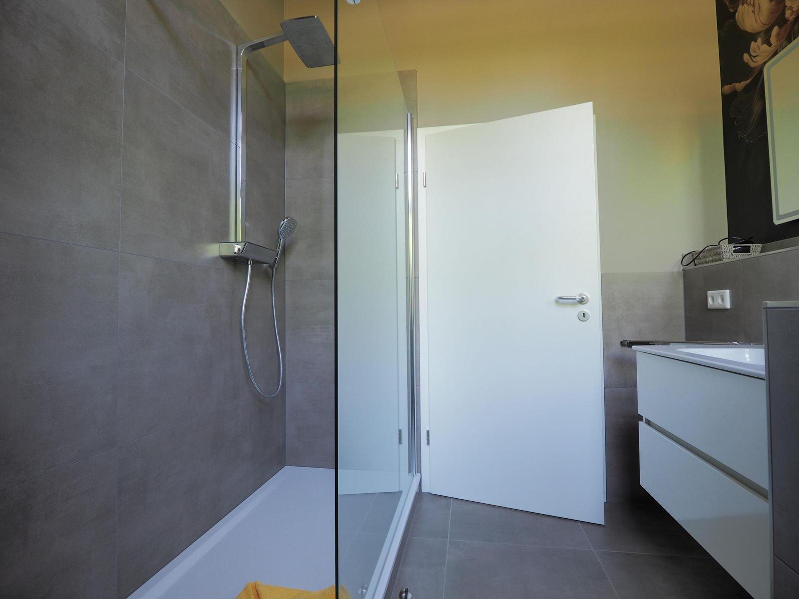 Duschkabine mit Glaswand, Waschbecken und Schrank in moderner Badezimmerausstattung.