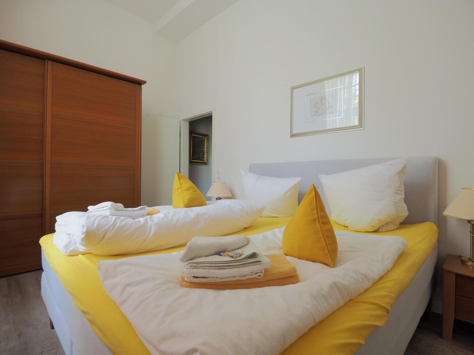 Ein Schlafzimmer mit Bett, Schrank und Nachttisch. Auf dem Bett liegen Handtücher und Kissen.
