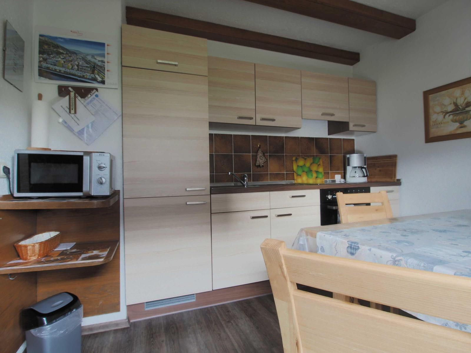 Kitchen with wooden furniture, microwave, coffee machine, and dining table with tablecloth.