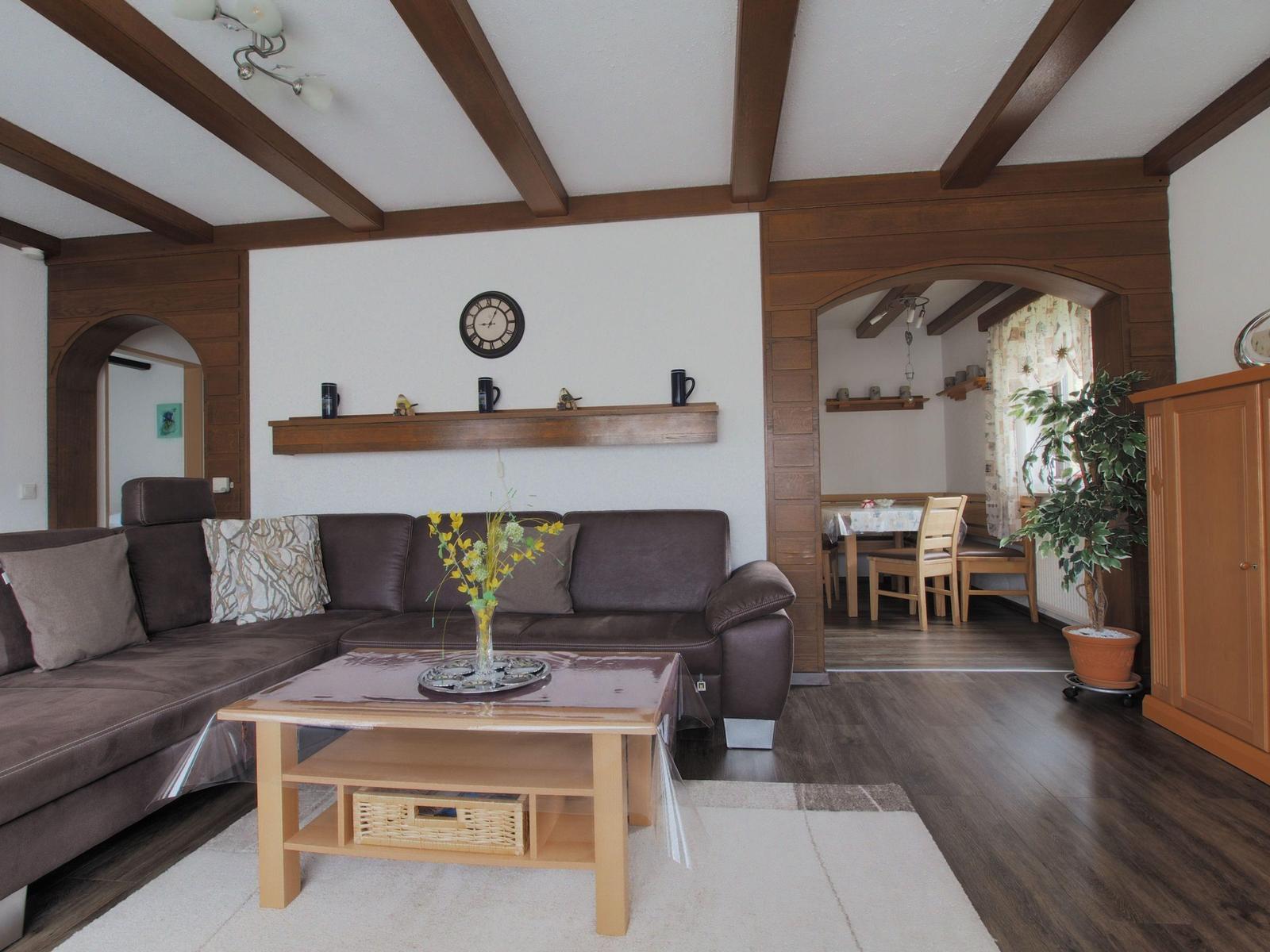 Living room with brown sofa, wooden beams, and table. Passage to dining area.