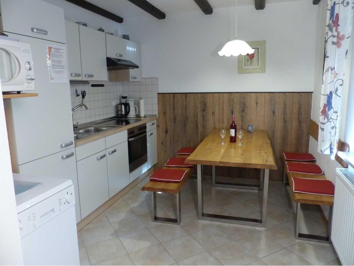 Kitchen with dining area, wooden table, benches with red cushions, and kitchen counter.