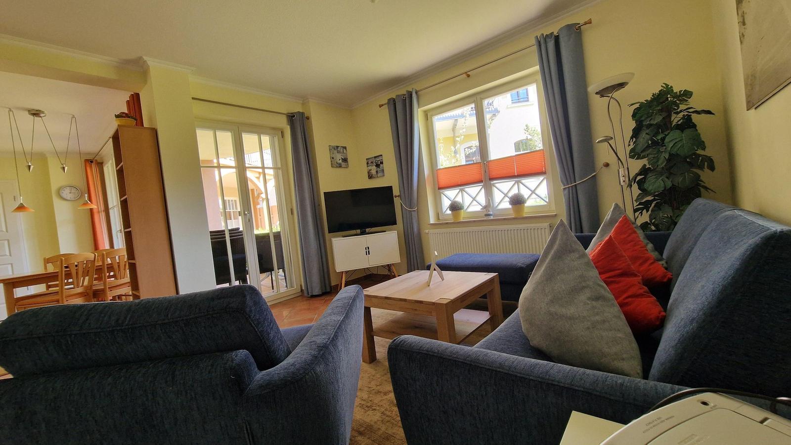 Wohnzimmer mit Sofa, Couchtisch und Fernseher. Durchgang zum Esszimmer und Terrasse.