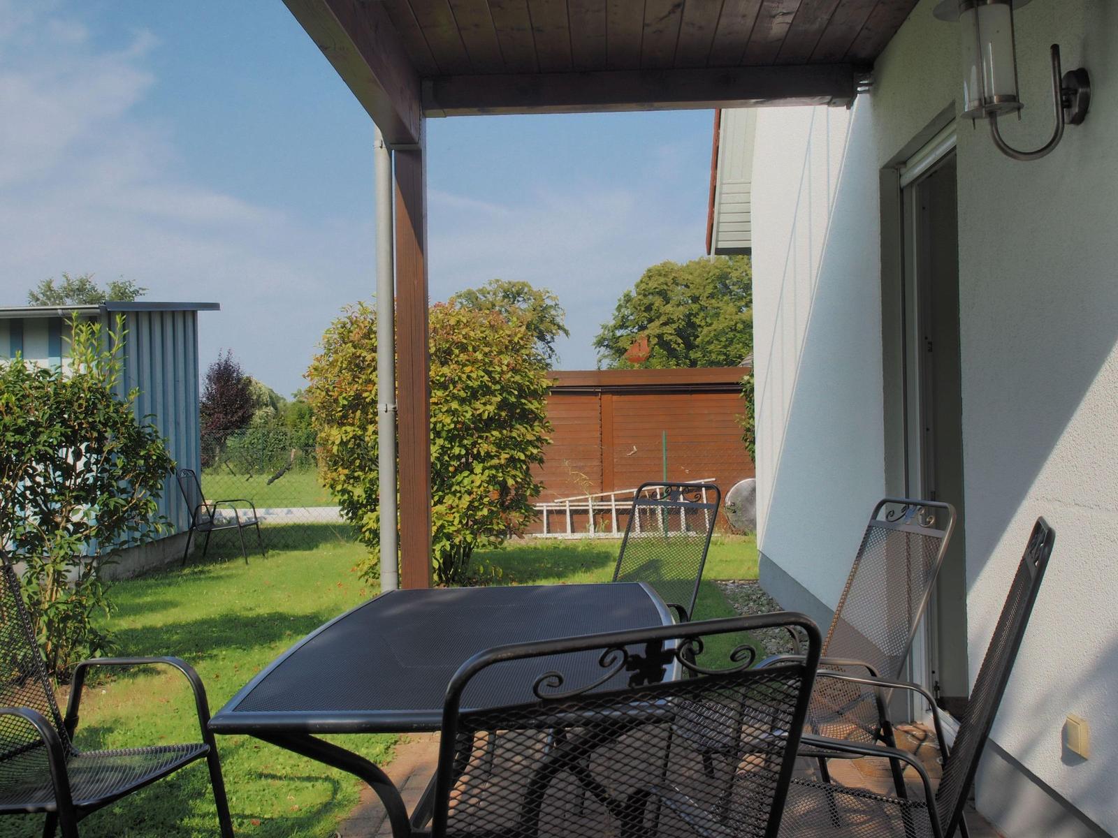 Terrasse mit Tisch und Stühlen, Blick auf grünen Garten und Zaun.