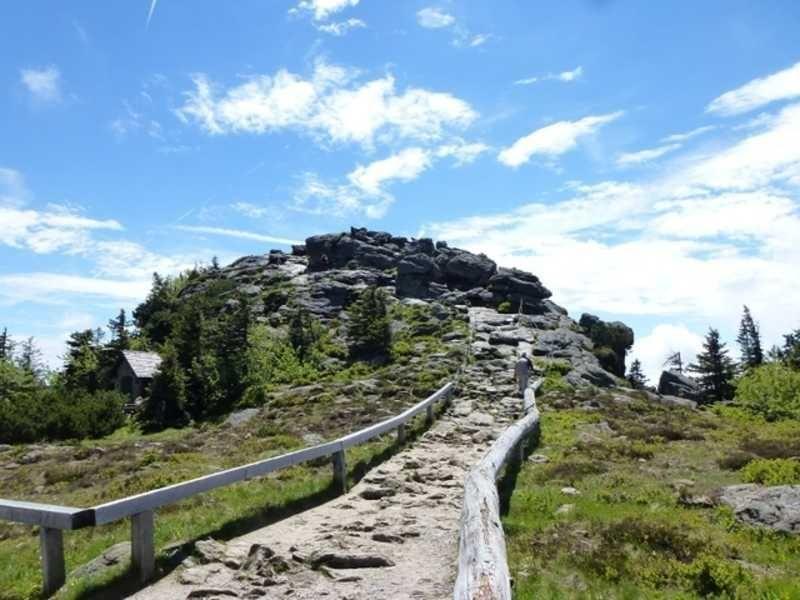Stone path leads to a mountain with rocks and forest under blue sky.