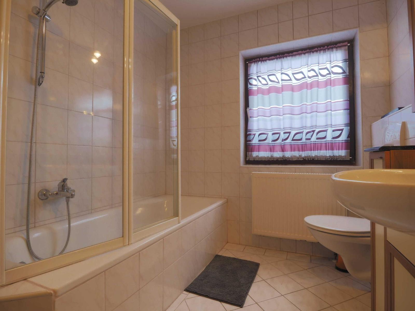 Bathroom with bathtub, shower, sink, and toilet. Window with curtain.