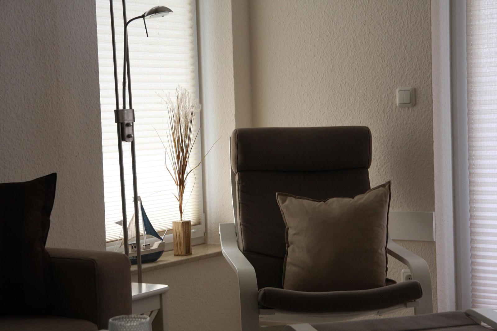 Ein Sessel mit Kissen steht vor einem Fenster mit Jalousie. Neben ihm steht eine Stehlampe.