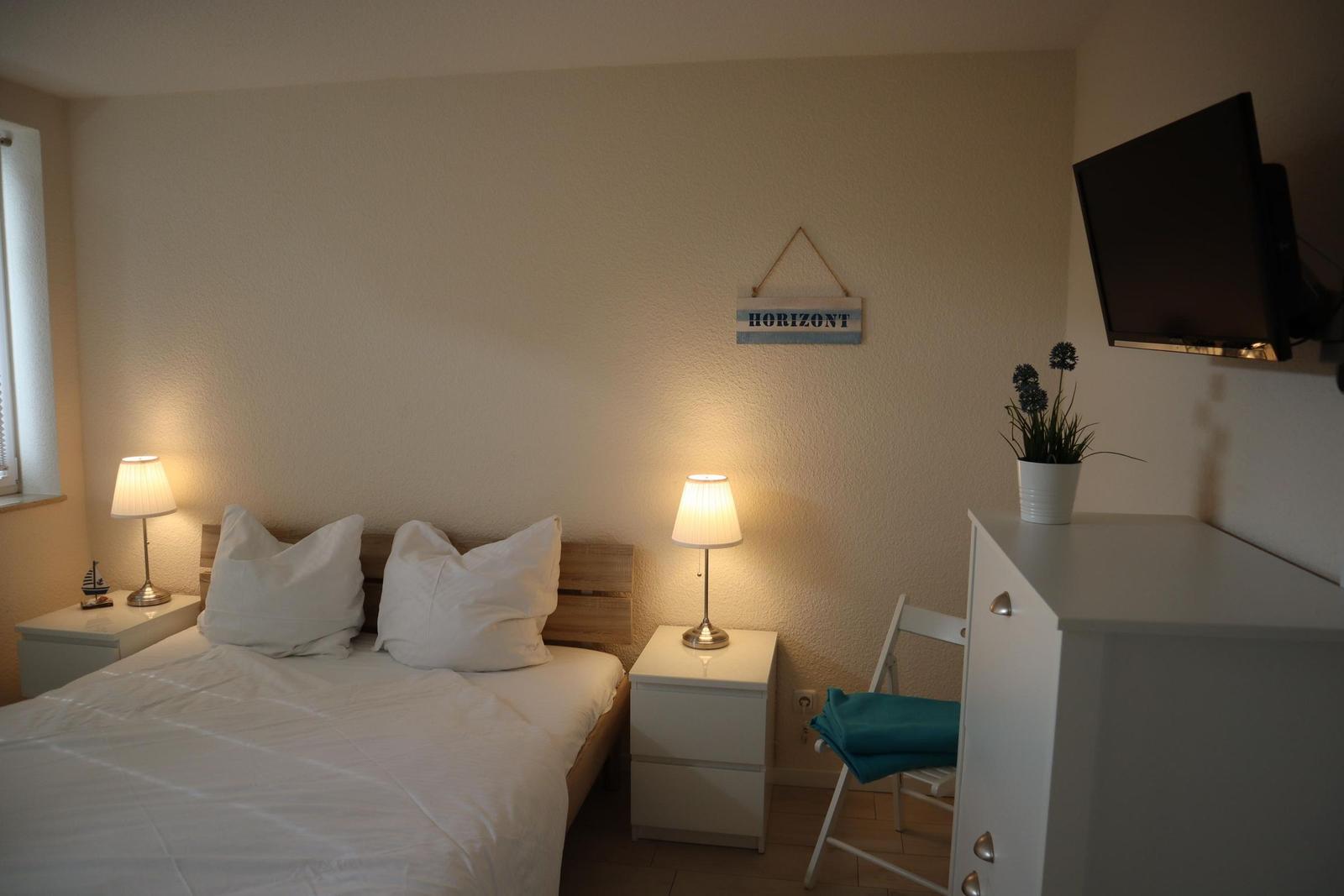Schlafzimmer mit Bett, Nachttischen, Fernseher und Pflanze.