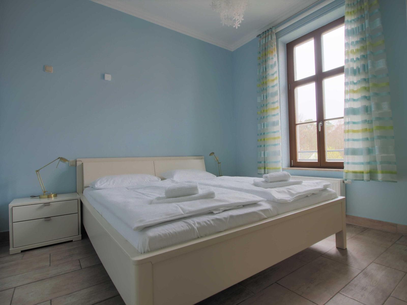 Schlafzimmer mit Doppelbett, Fenster und Nachttisch.