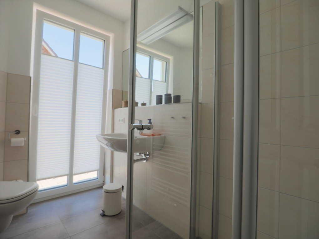 Badezimmer mit Dusche, Waschbecken und Toilette. Fenster mit Jalousie.