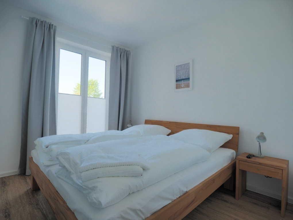 Schlafzimmer mit Holzbett, Fenster und Nachttisch.