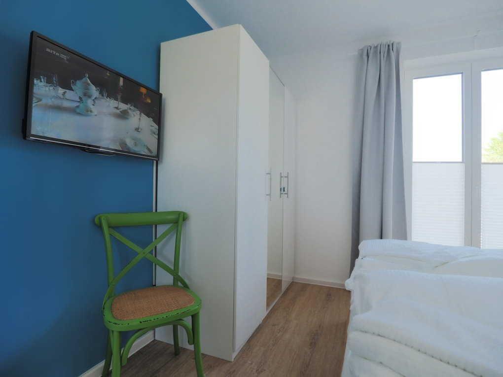 Schlafzimmer mit Bett, Kleiderschrank, TV und grüner Stuhl.