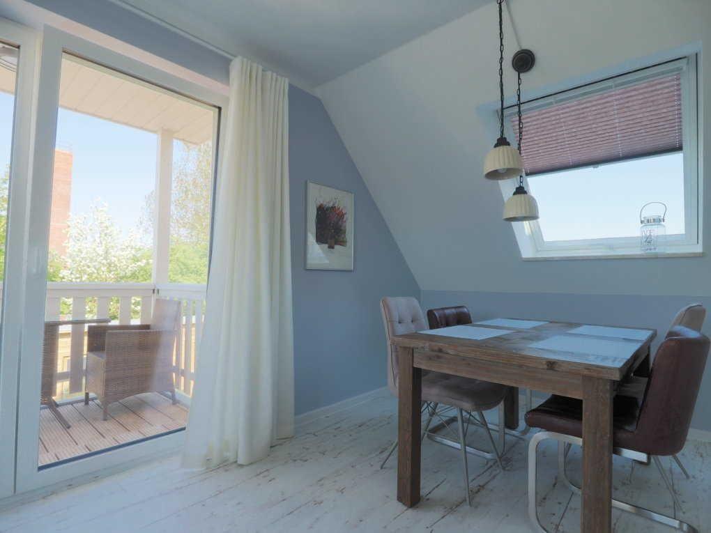 Esszimmer mit Tisch, Stühlen und Blick auf Balkon. Wandfarbe blau-weiß.