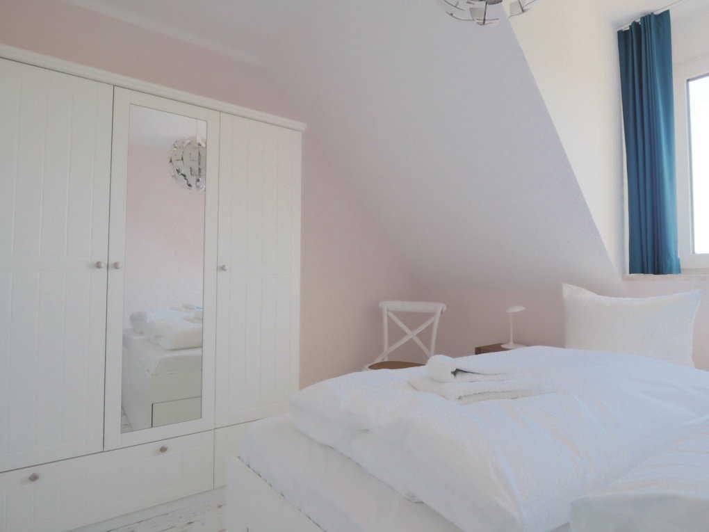 Schlafzimmer mit weißem Bett, Kleiderschrank und blauen Vorhängen an einem Fenster.