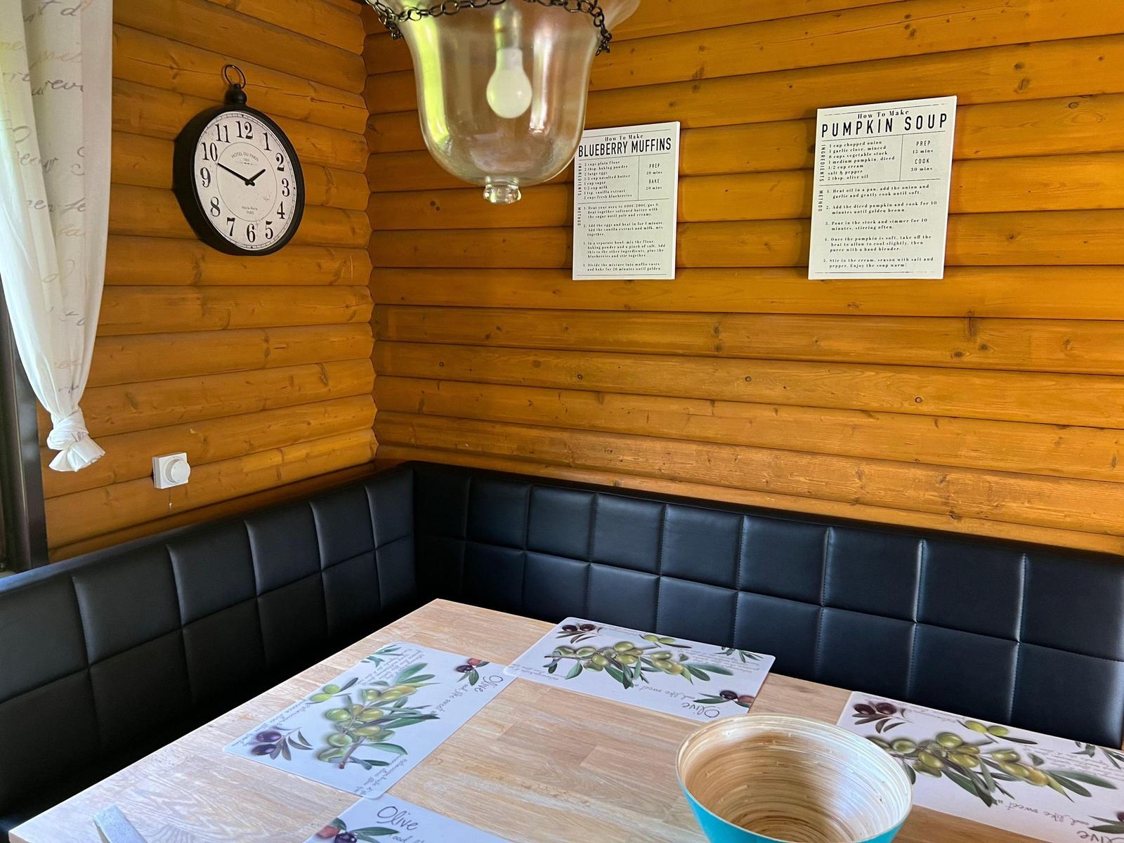 Dining area with wooden walls, black cushioned benches, and table with olive motifs.