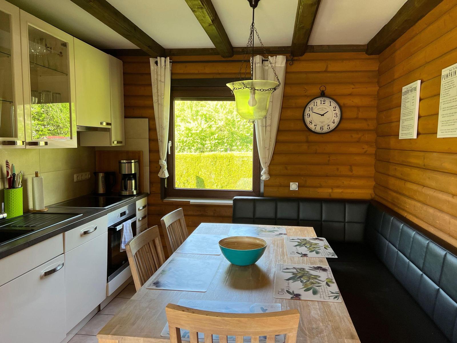 Kitchen with dining area, wooden walls, table, chairs, and window with garden view.
