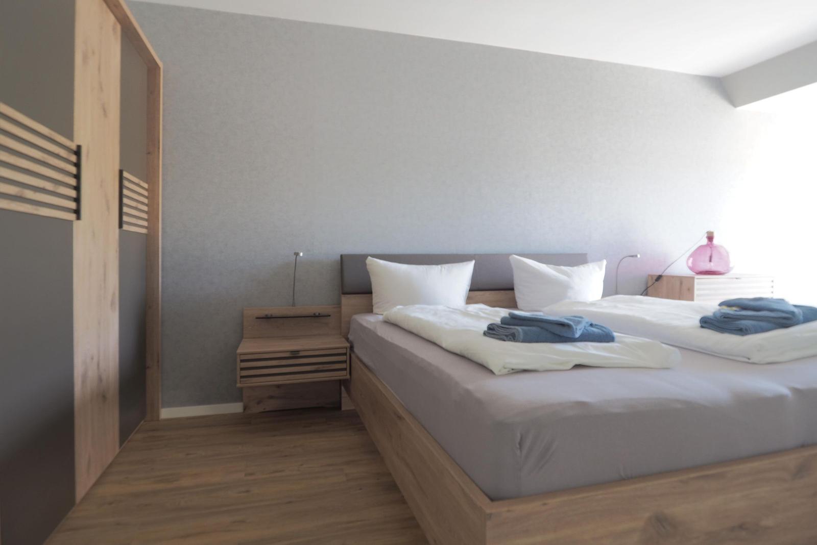 Schlafzimmer mit Bett, Nachttisch und Kleiderschrank. Holzboden und graue Wand.
