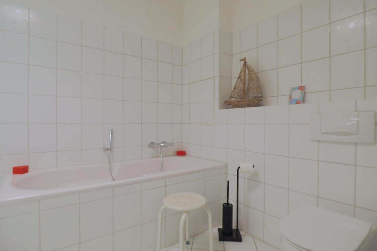Bad mit Badewanne, Toilette und kleinem Regal mit Segelboot.