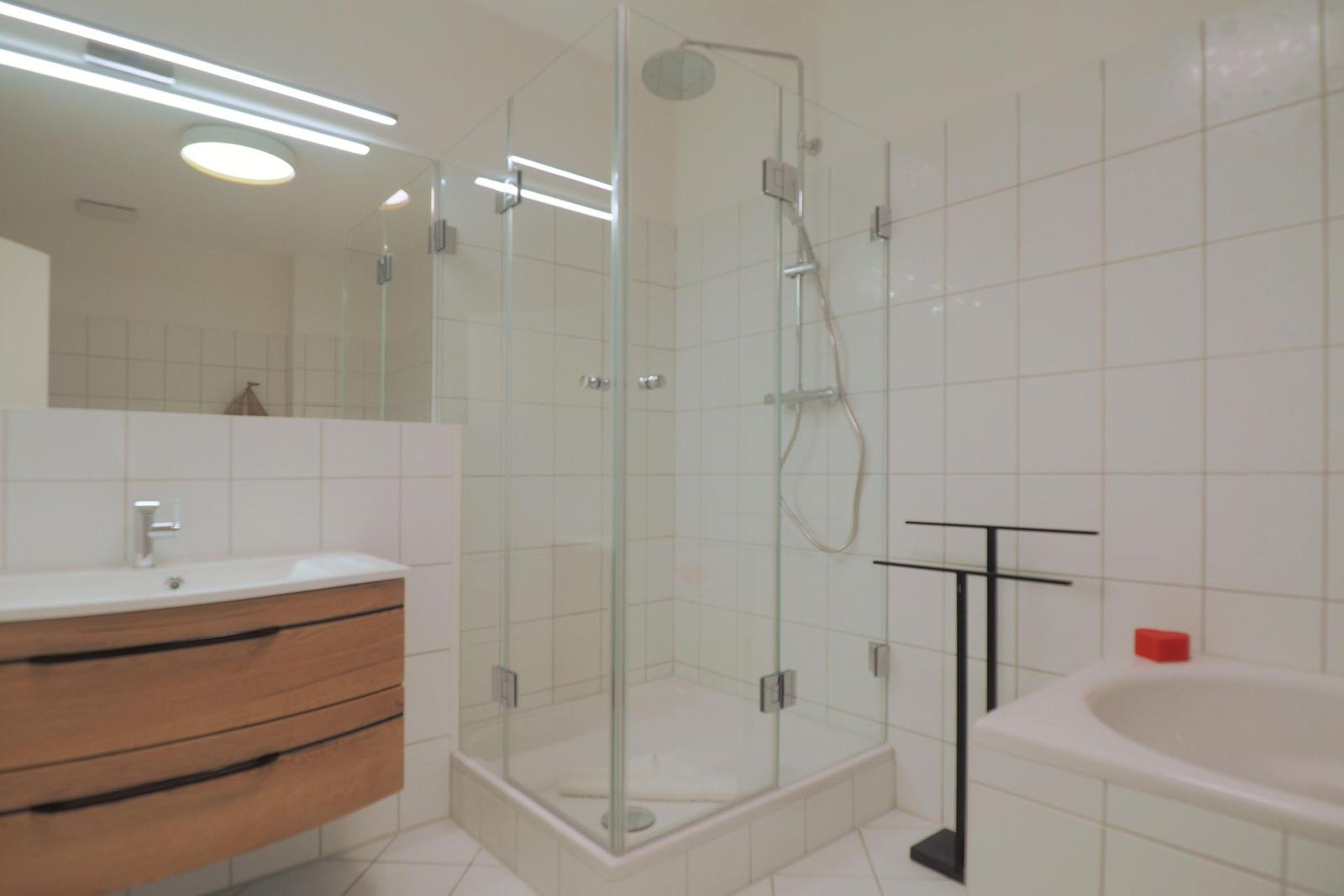 Badezimmer mit Dusche, Badewanne und Waschbecken mit Holzschrank.
