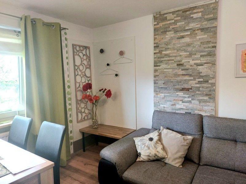 Living room with sofa, table, chairs, and stone wall. Window with green curtains.