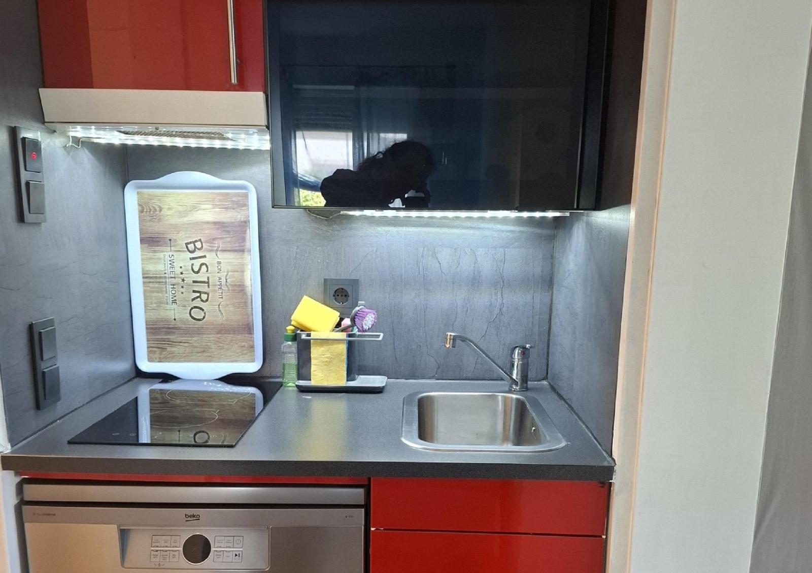 Kitchen with sink, stove, and dishwasher. Red-black fronts and illuminated worktop.