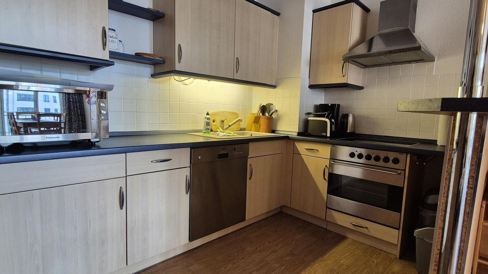 Küche mit Edelstahlgeräten, Holzschrankfronten und dunkler Arbeitsplatte.