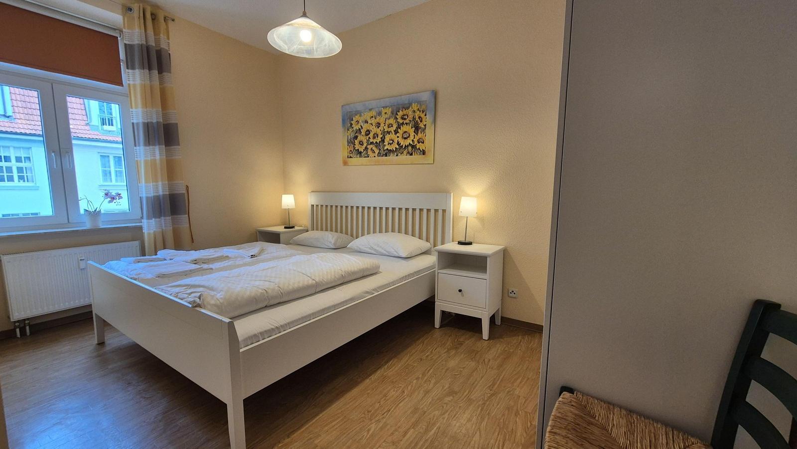 Schlafzimmer mit Doppelbett, Nachttischen und Fenster mit Blick auf Gebäude.