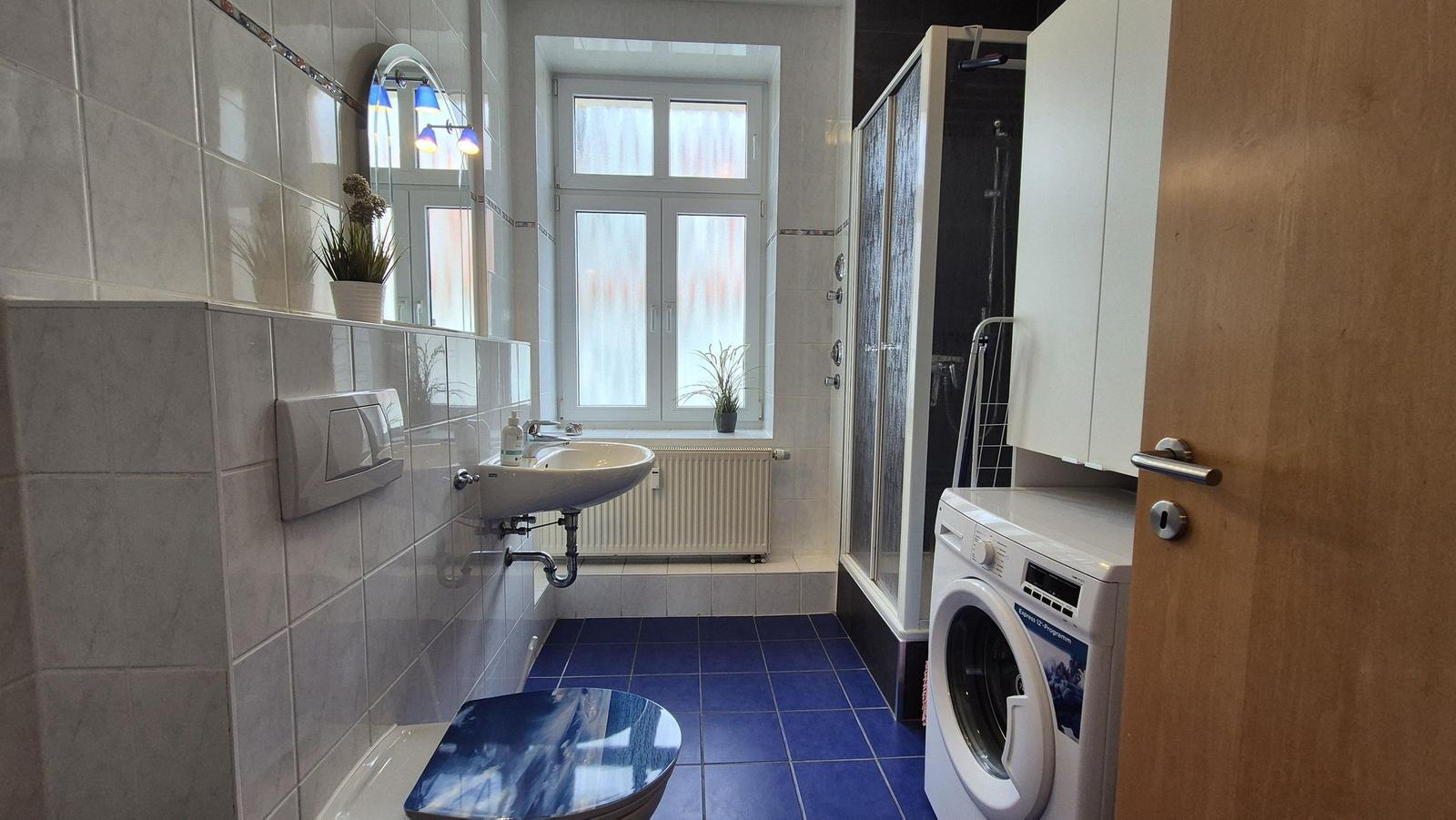 Badezimmer mit Dusche, Waschmaschine und Fenster.