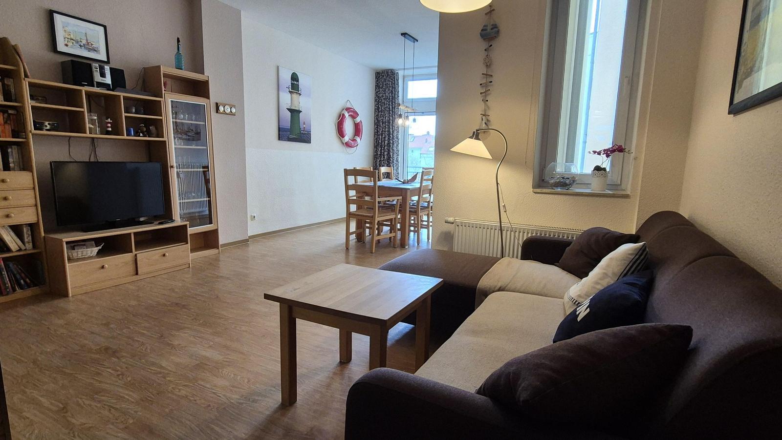 Wohn- und Essbereich mit Sofa, Tisch und Fernseher. Wandbild und Rettungsring sichtbar.