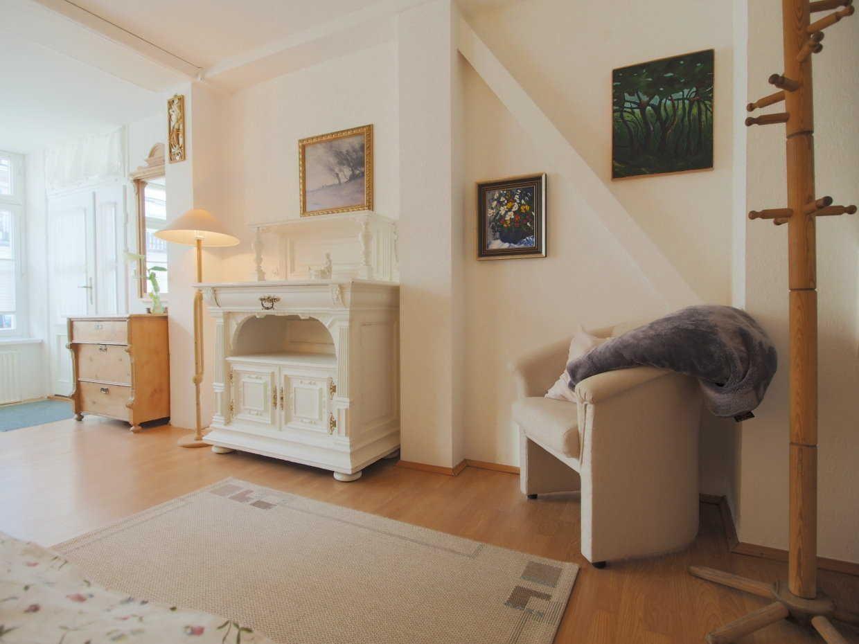 Wohnzimmer mit weißem Schrank, Sessel, Kleiderständer und Bildern an der Wand.