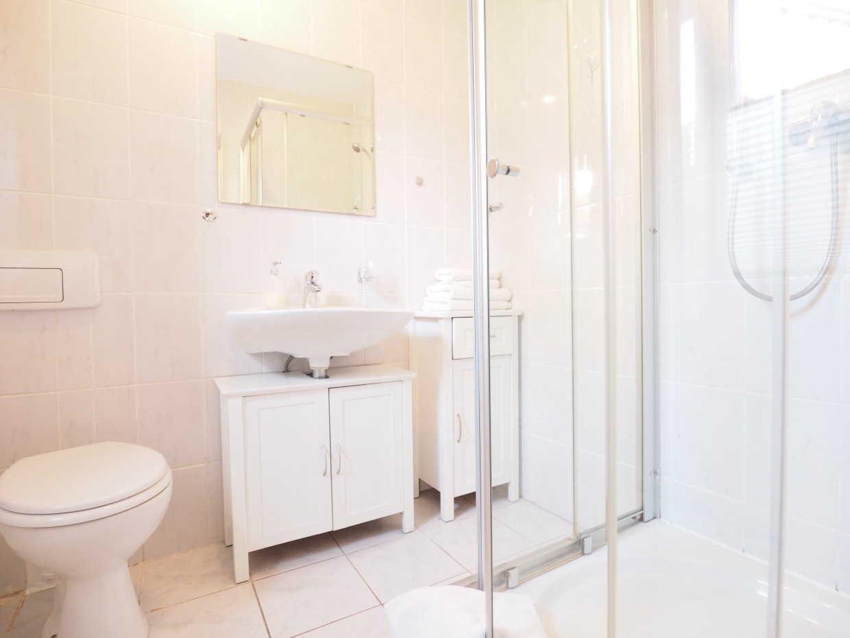 Badezimmer mit Dusche, Waschbecken und Toilette. Weiße Fliesen und Möbel.