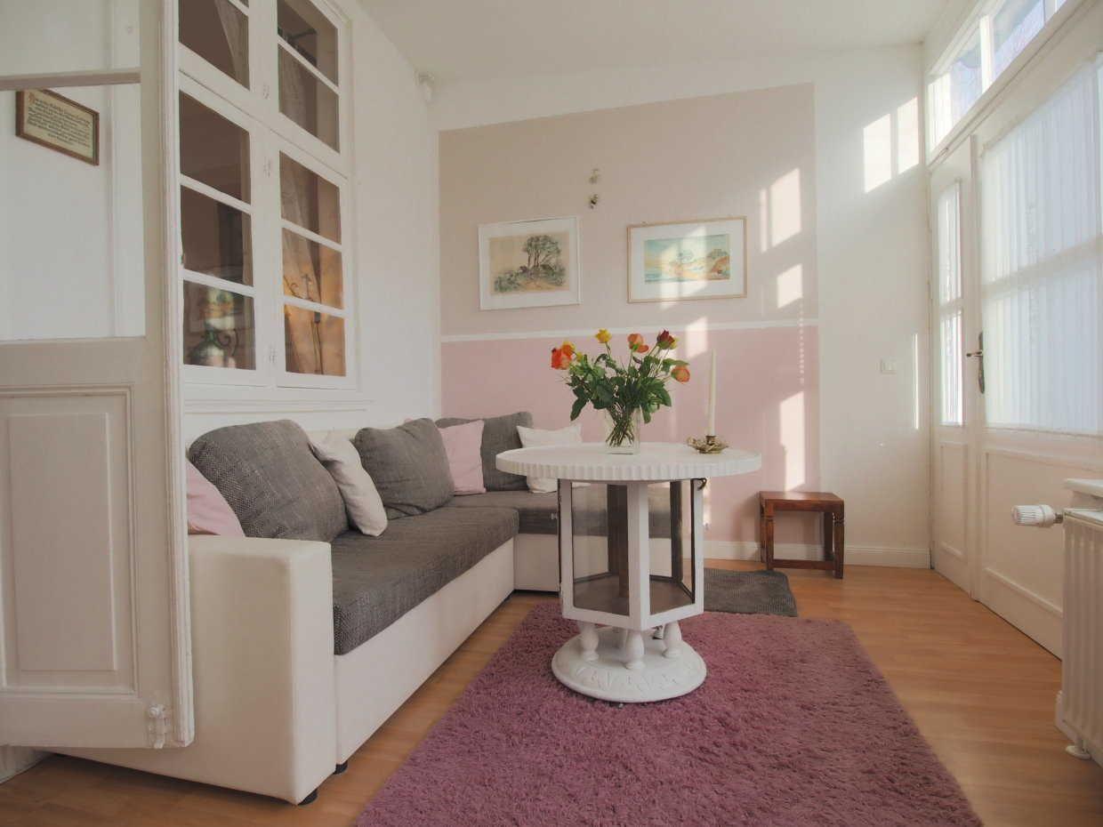 Wohnzimmer mit Sofa, runden Tisch und Blumen. Wand in Rosa-Beige-Ton.