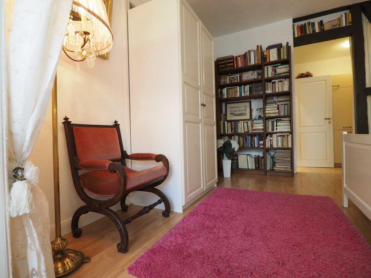 Ein Raum mit einem roten Sessel, einem Bücherregal und einem pinken Teppich.
